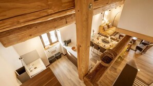 Une cuisine moderne avec des poutres en bois, un coin repas avec un canapé jaune et une vue sur le salon situé en contrebas.