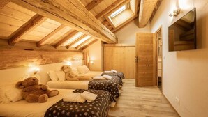 Une chambre confortable située sous les toits, avec des poutres apparentes, une grande fenêtre et un téléviseur fixé au mur.