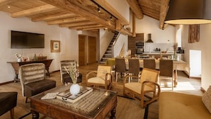 Un vaste espace de vie doté d’un plafond en bois, d’une table à manger dressée pour six personnes et d’une cuisine située au fond de la pièce.