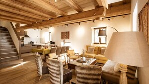 Un vaste espace de vie agrémenté de poutres en bois, comprenant un canapé, des fauteuils, une table basse et une table à manger.