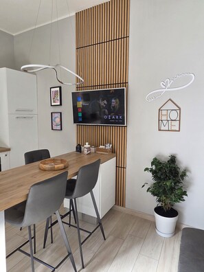 Une cuisine moderne avec une table à manger en bois, des chaises, un téléviseur fixé au mur et une plante en pot.