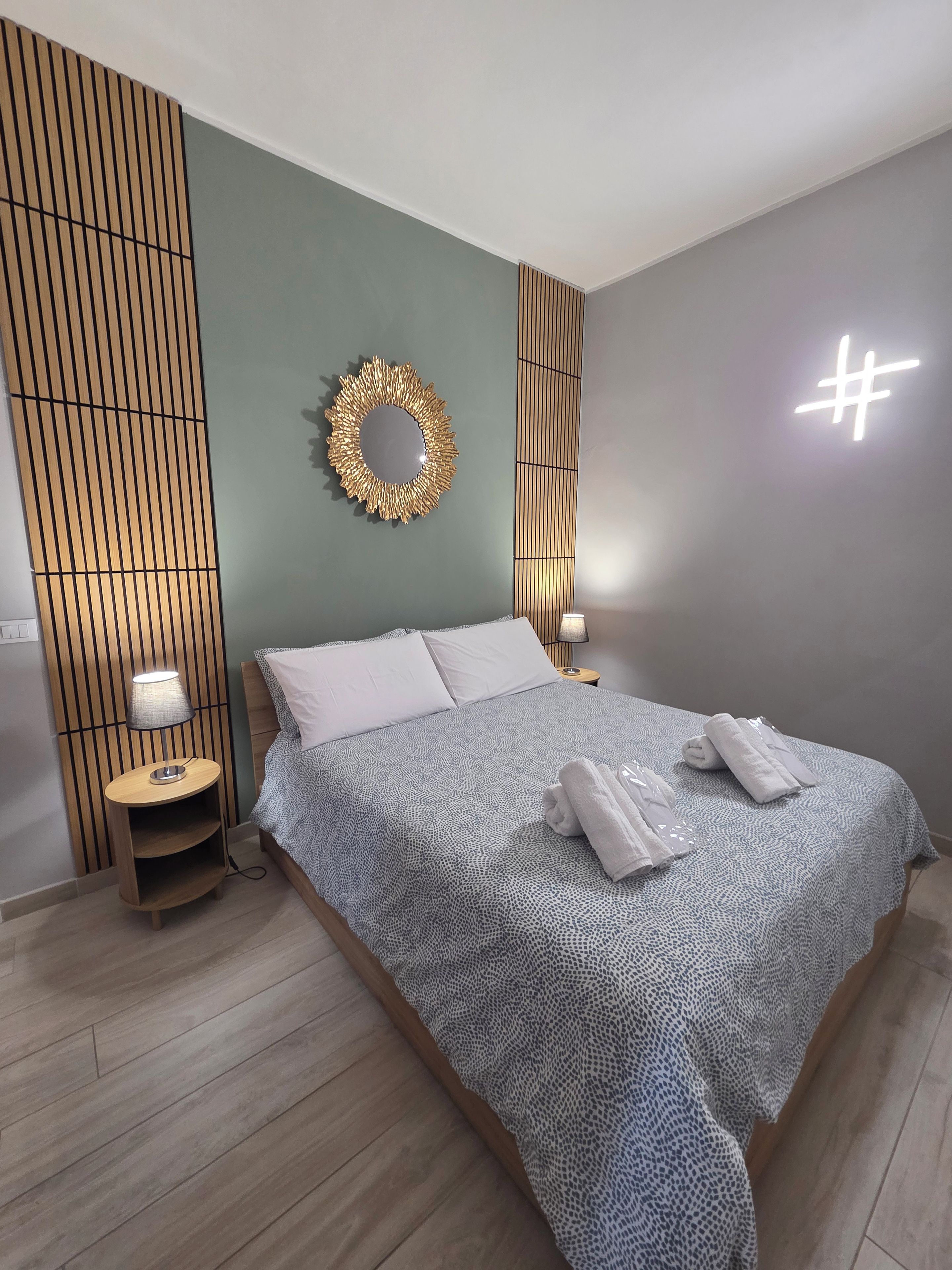 Una camera da letto moderna con un letto, comodini, una lampada e un pannello decorativo a parete.