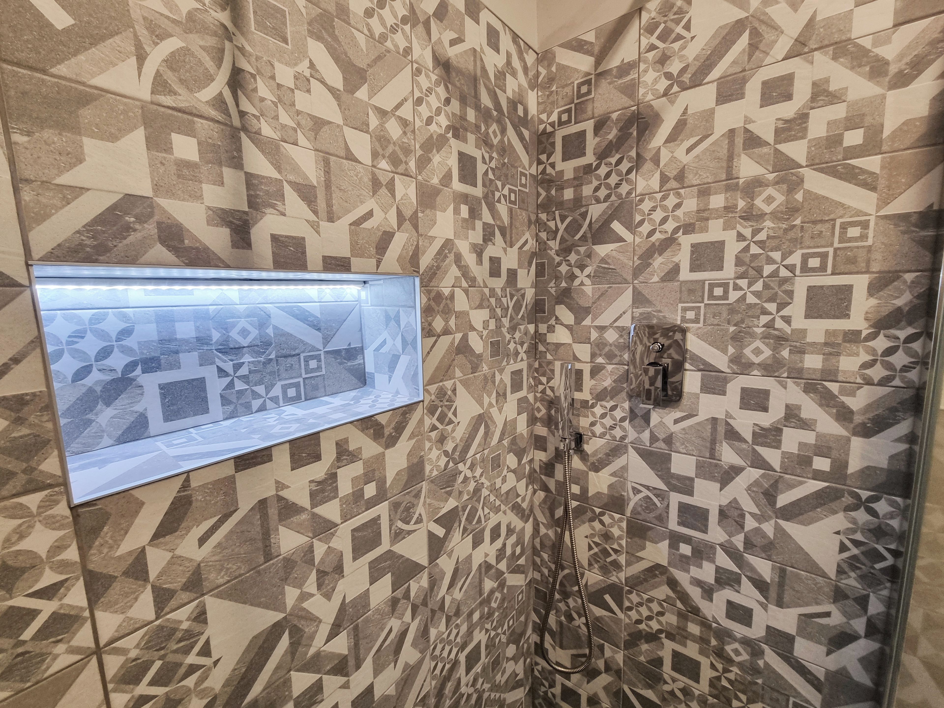 Une salle de bain avec des carreaux décorés, une fenêtre et une douche.