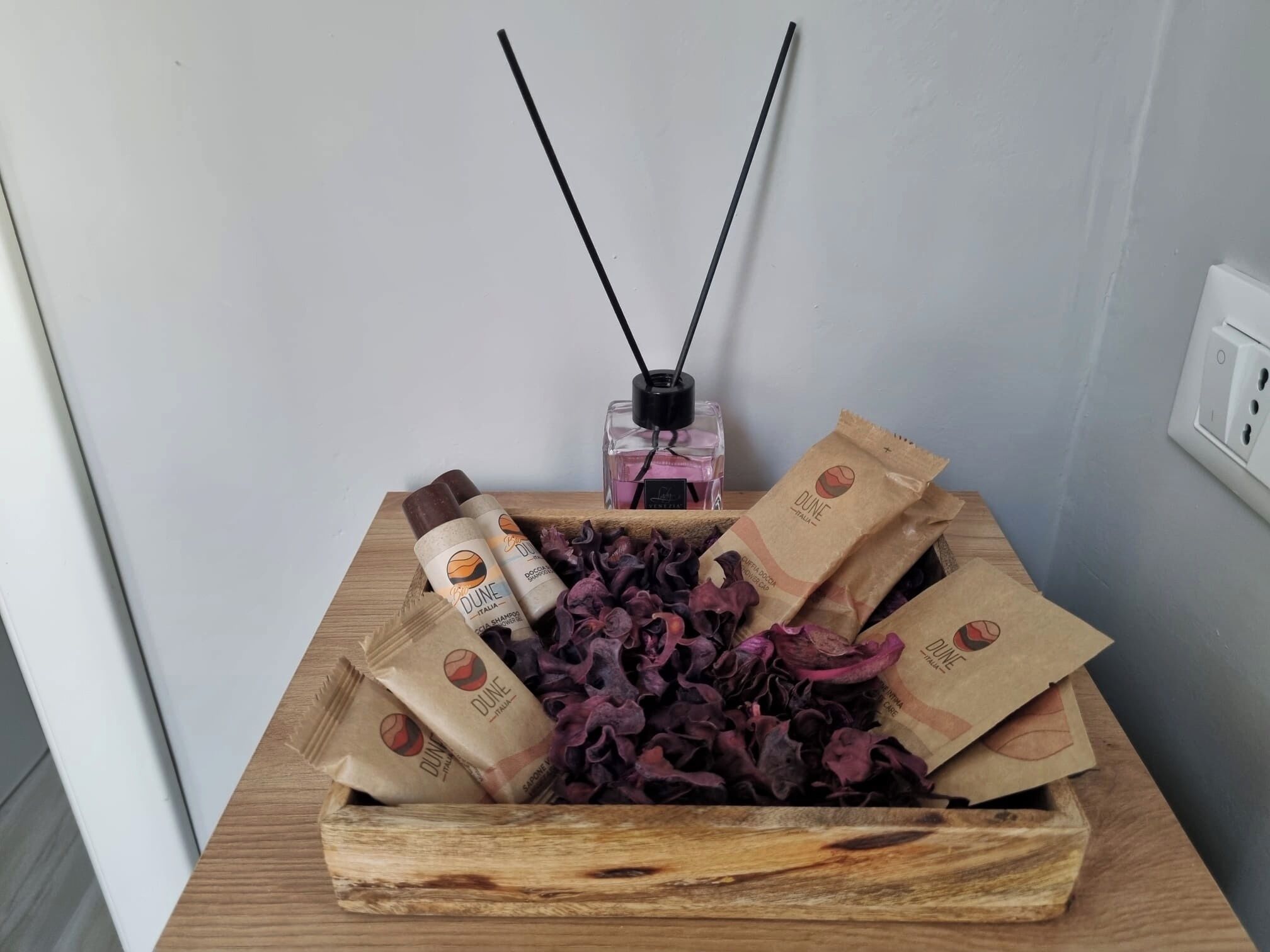 A wooden box containing dried flowers, a diffuser, and two bottles of Dune Italy shampoo.