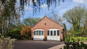 A brick house with a white garage door, surrounded by greenery and trees. - Cosy and Secluded Brook-side Lodge (Sleaford)