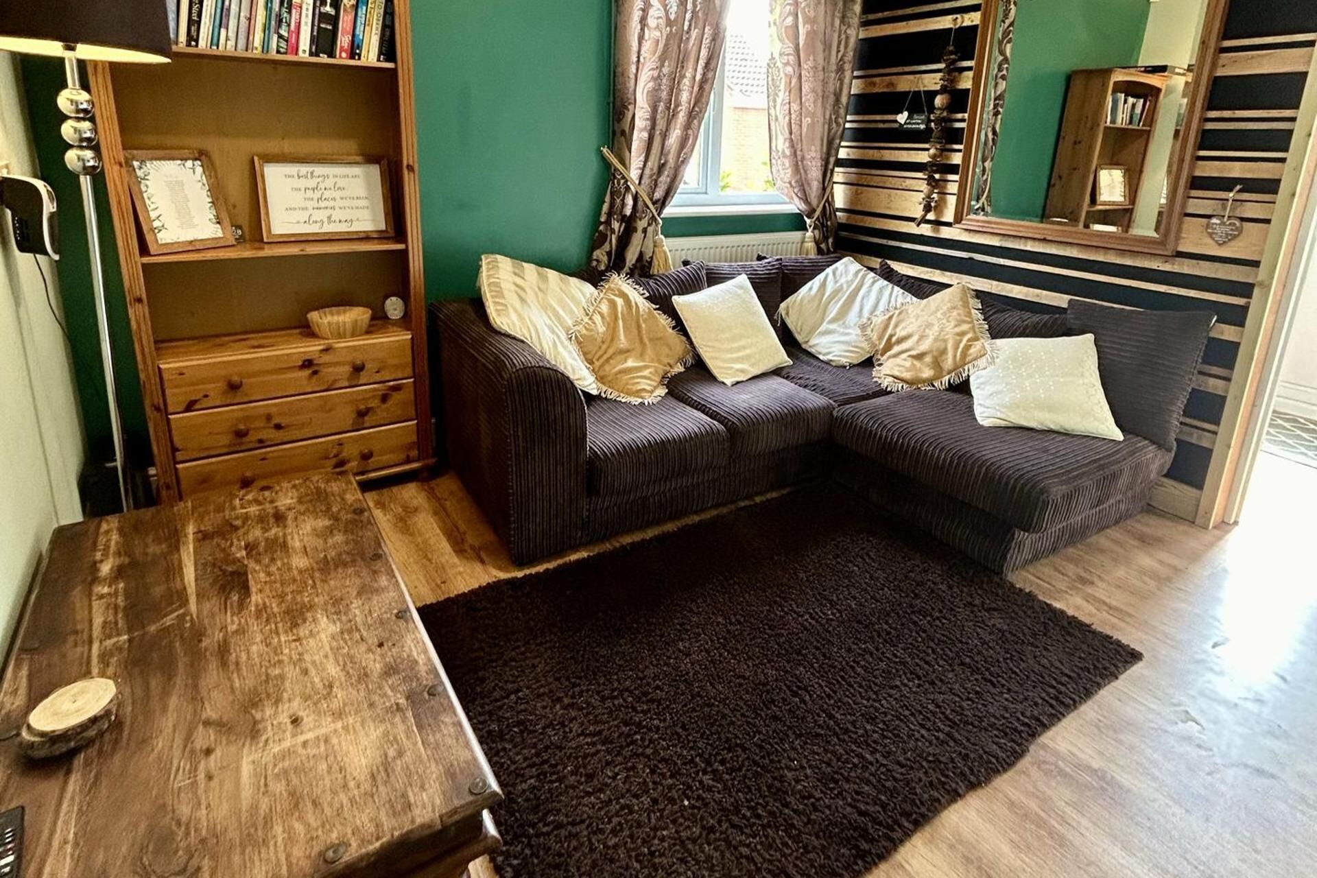 A cozy living room with a sectional sofa, a wooden coffee table, and a bookshelf filled with books.