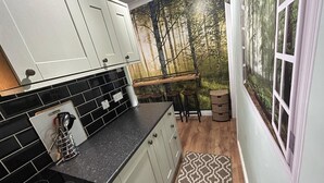 A kitchen with white cabinets, black tiles, and a large window with a forest mural. - Cosy and Secluded Brook-side Lodge (Sleaford)