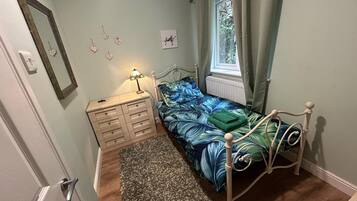 Ett sovrum med en säng, en byrå, ett nattduksbord, ett fönster med gardiner och en vägg dekorerad med hjärtformade prydnader.
