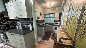 A compact kitchen with white cabinets, a black countertop, and a wooden bar area. - Cosy and Secluded Brook-side Lodge (Sleaford)