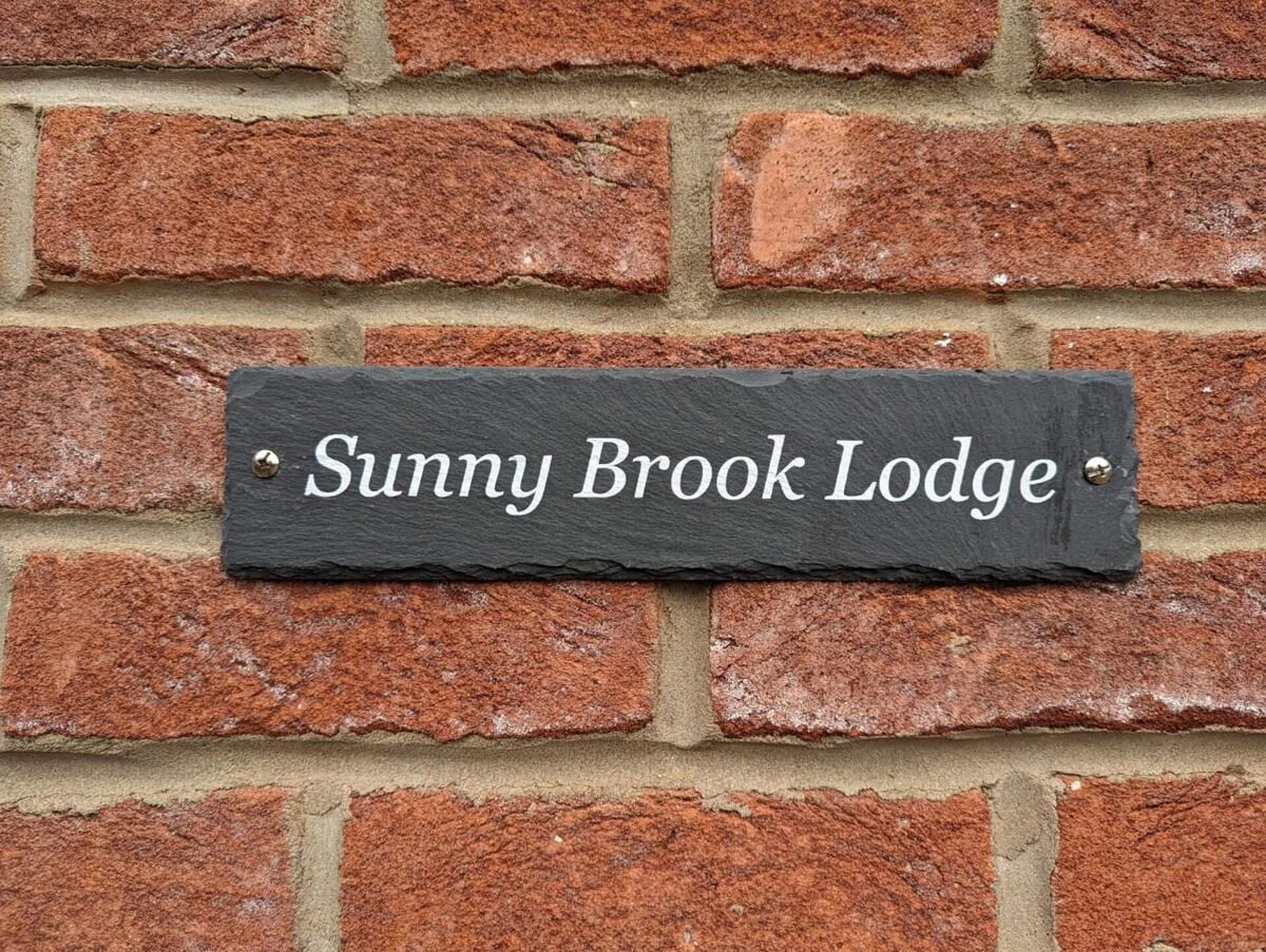 A slate sign with the text "Sunny Brook Lodge" mounted on a brick wall.