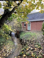 A brick house with a small front yard, a wooden fence, and a narrow stream.