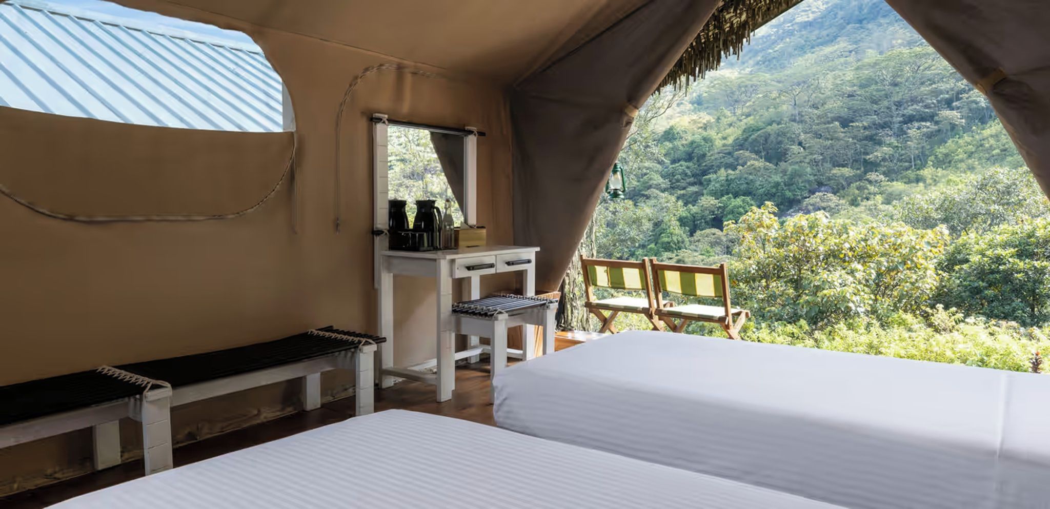 A bedroom with a bed, a desk, a bench, and a chair with a view of a forest.