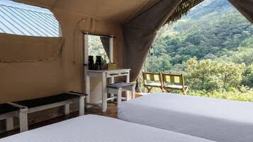 A bedroom with a bed, a desk, a bench, and a chair with a view of a forest.