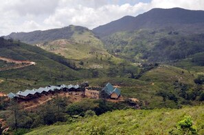 A series of wooden cabins with sloped roofs in a hilly, green landscape. - Wild Glamping Knuckles - Thema Collection (Galgamuwa)