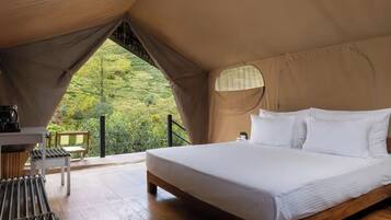 A tented accommodation with a bed, bedside table, and a view of greenery.