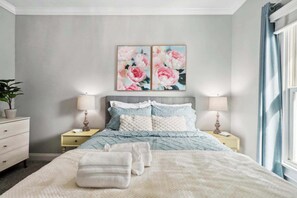 A bedroom with a bed, two nightstands, a dresser, and a large window with curtains. - Charming Home | Victorian District (Savannah)