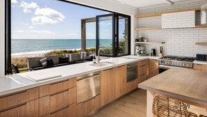 Una cocina moderna con un amplio ventanal con vistas a la playa, armarios de madera, un lavamanos de acero inoxidable y una estufa a gas.