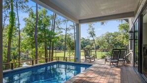 Piscina exterior cubierta con plataforma de madera, rodeada de árboles y vista a un campo de golf.