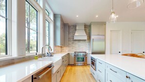 Una cocina moderna con armarios blancos, una estufa de acero inoxidable y un amplio ventanal que proporciona luz natural.