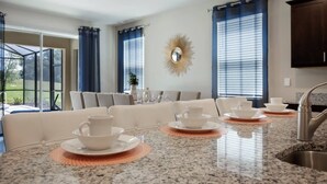 Une cuisine moderne dotée de plans de travail en granit, d’un évier en acier inoxydable et d’un coin repas avec une grande table dressée pour quatre personnes.