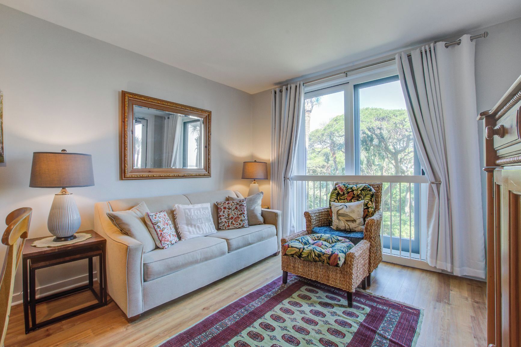 Un salon avec un canapé, un fauteuil, un tapis, une lampe, un miroir et une fenêtre avec des rideaux.