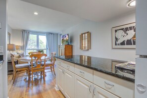 A kitchen with a dining area, wooden cabinets, a window with curtains, and a framed artwork on the wall.
