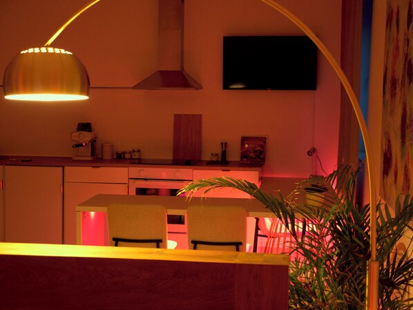Una cocina con comedor, un televisor montado en la pared y una planta al frente.