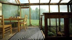 Un invernadero con una mesa y sillas de madera, un tapete a rayas blanco y negro, y plantas en macetas.