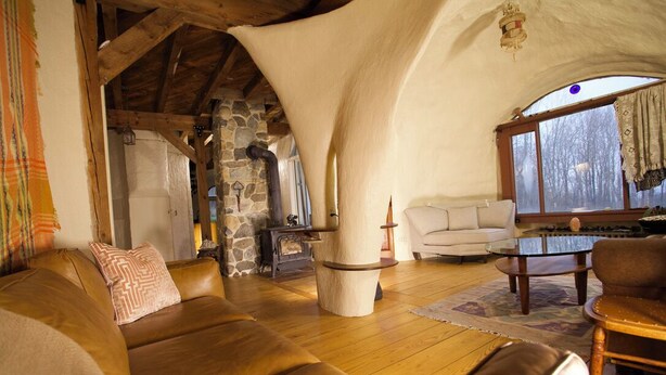 Una sala de estar acogedora con chimenea de piedra, sofá de cuero y un ventanal con vistas a árboles.