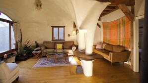 Una sala de estar acogedora con techo de madera, un sofá de cuero marrón, una mesa de centro redonda y un pilar blanco grande.