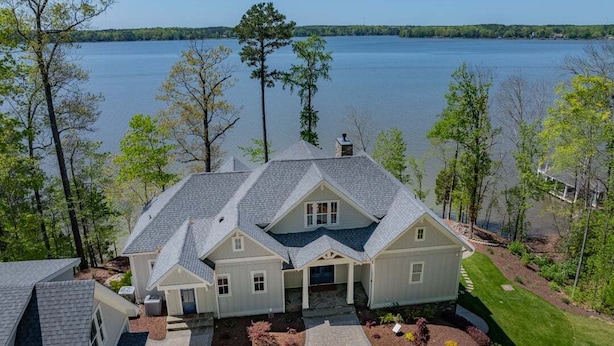 Une grande maison dotée d’un patio abrité, entourée d’arbres et bordée d’un lac.
