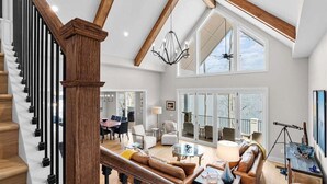 Un vaste espace de vie agrémenté d’un escalier en bois, d’un lustre et de grandes fenêtres.