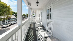 Une véranda blanche avec une balustrade, une chaise en osier et une table.