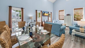 Un coin repas avec une table en verre, des chaises en osier et un canapé bleu en arrière-plan.