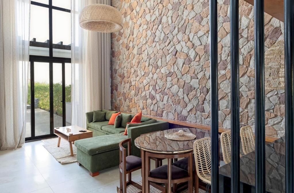 A modern living room with a stone wall, a green sofa, a round table, and wicker chairs.