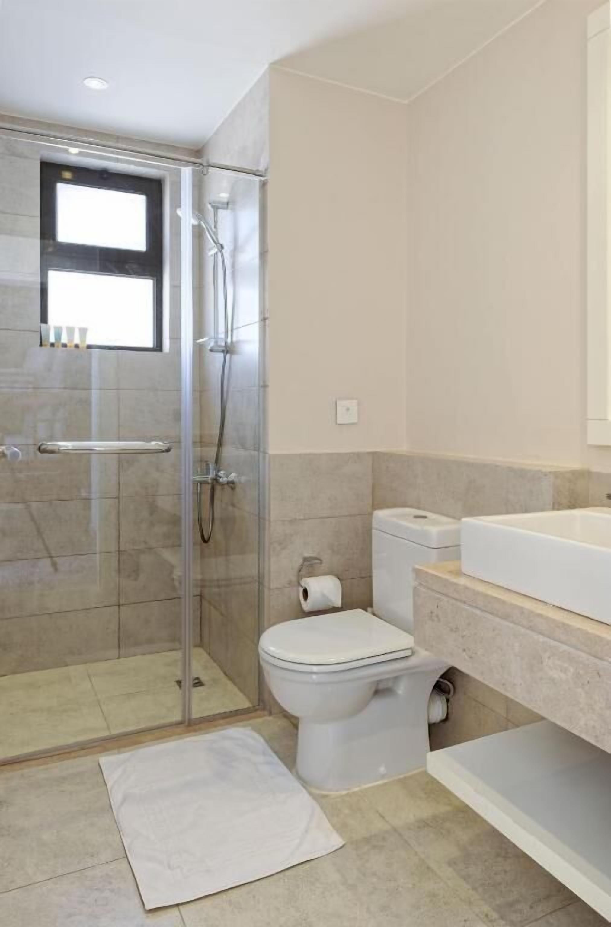 Et moderne badeværelse med en glasafskærmet brusekabine, toilet og håndvask.
