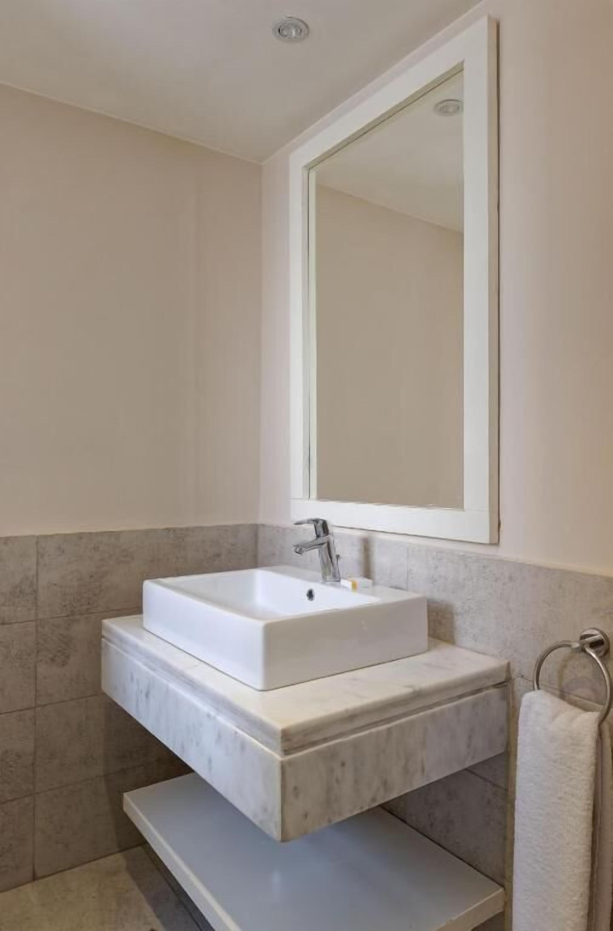 A bathroom with a white rectangular sink, a mirror above it, and a towel rack to the right.