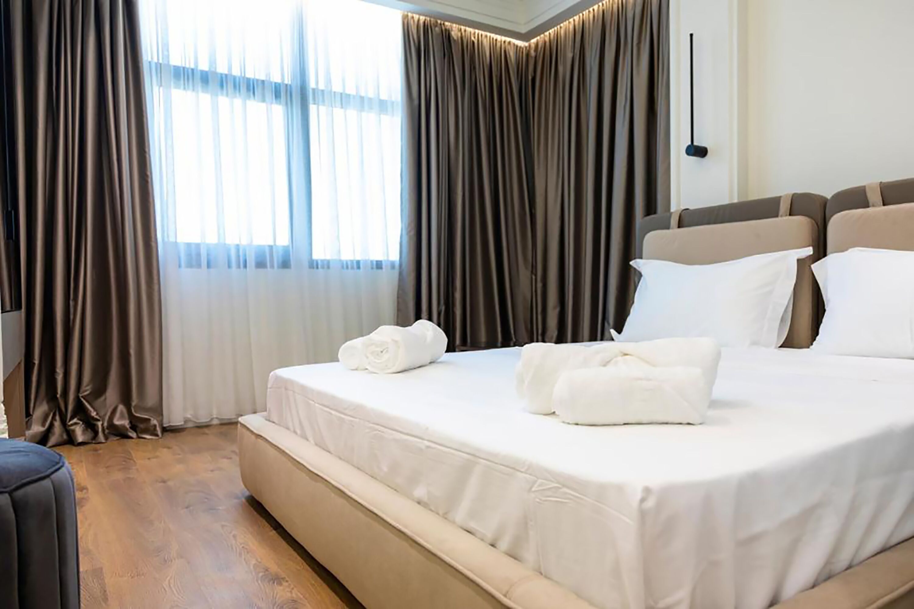 Una habitación de hotel con una cama grande, piso de madera y una ventana con cortinas.