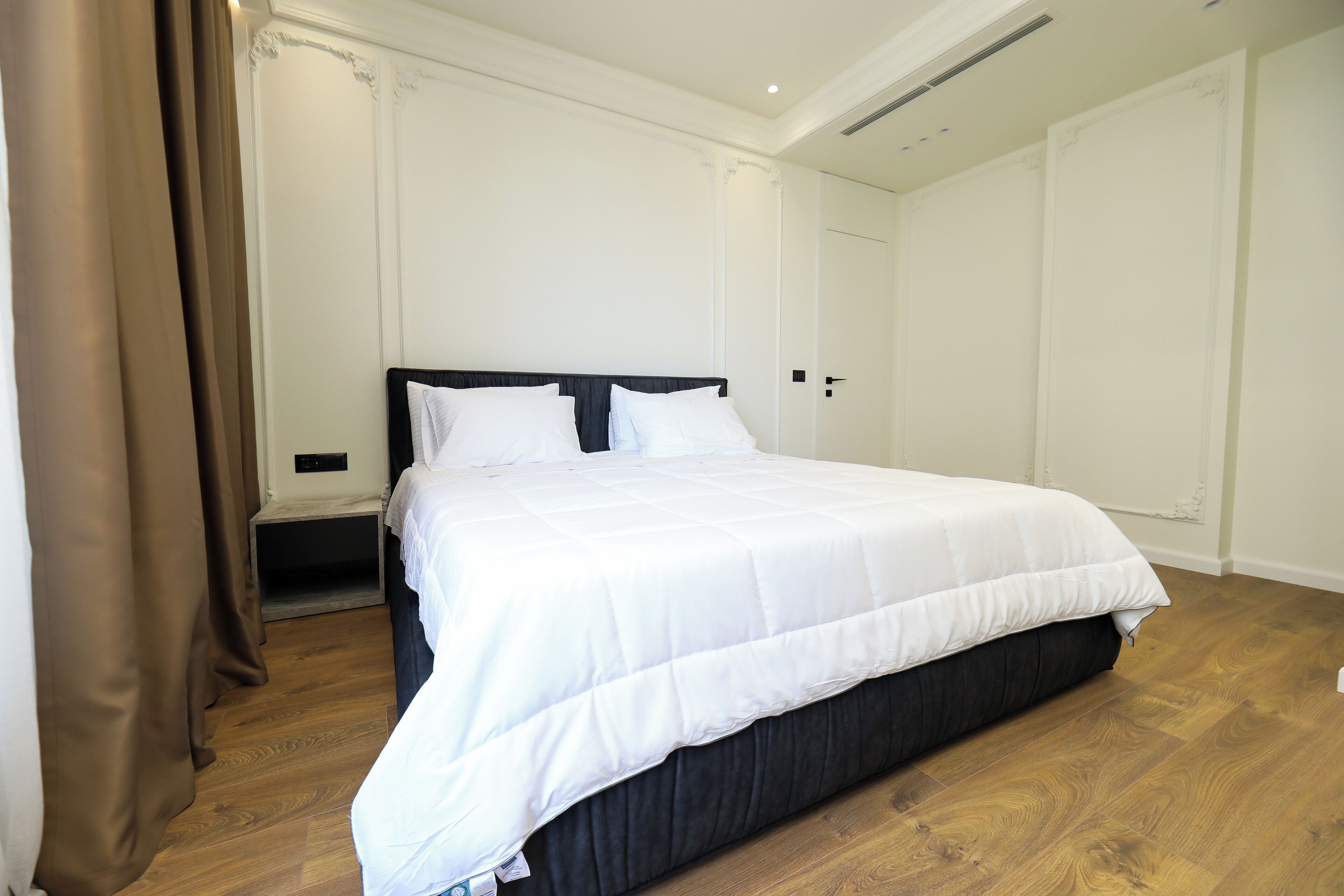A bedroom with a large bed, wooden flooring, and white walls.