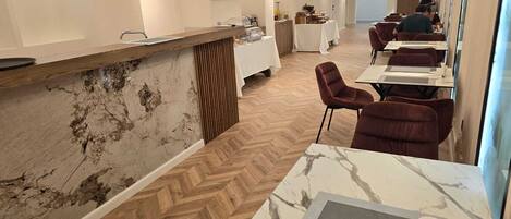 Un restaurante moderno con suelo de madera en espiga, mesas con cubierta de mármol y sillas tapizadas en rojo.