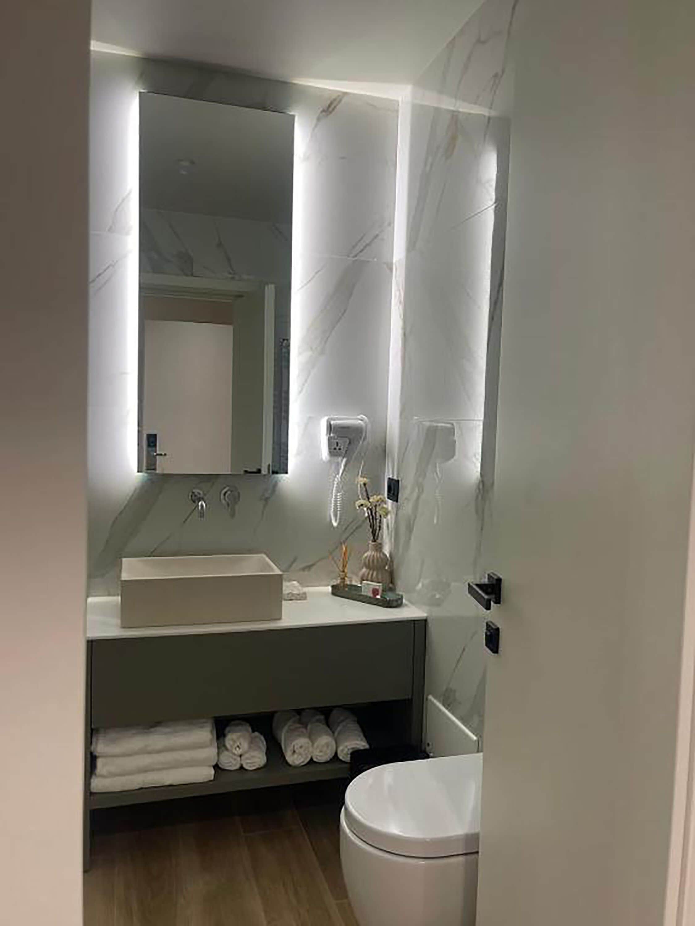A modern bathroom with a white vanity, a large mirror, and a toilet.