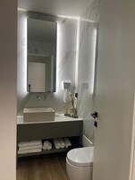 Un baño moderno con tocador blanco, un espejo grande y un inodoro.