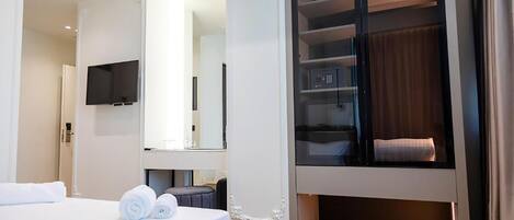 A modern hotel room with a bed, a TV, a walk-in closet, and a mirror.