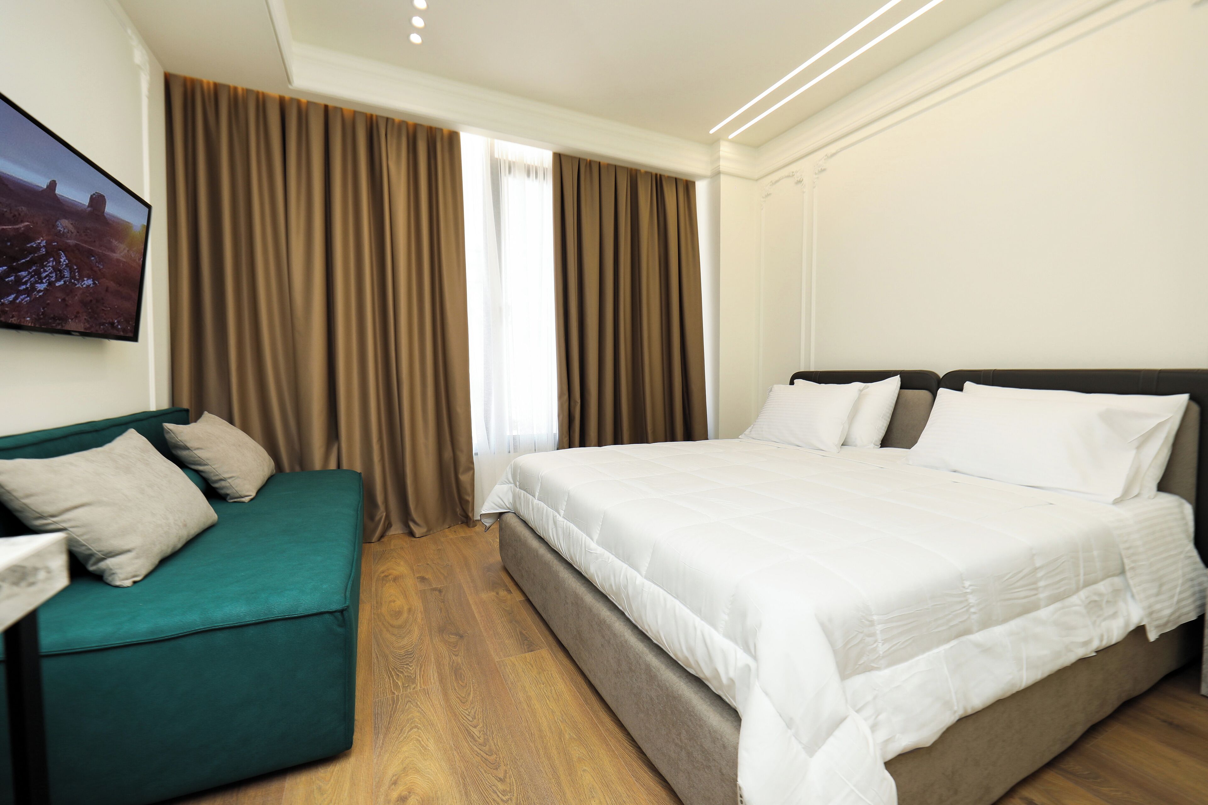 A hotel room with a bed, a green sofa, wooden flooring, and a large window with curtains.