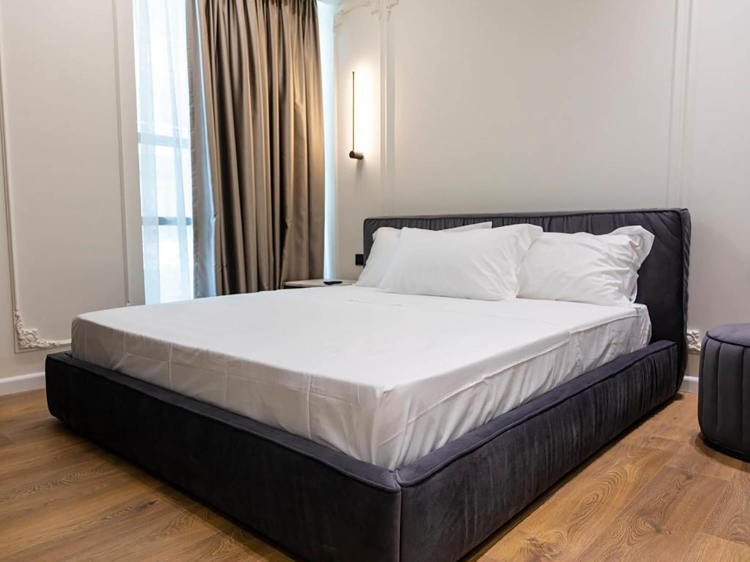 Una camera da letto moderna con un letto grande, pavimento in legno e una finestra con tende.