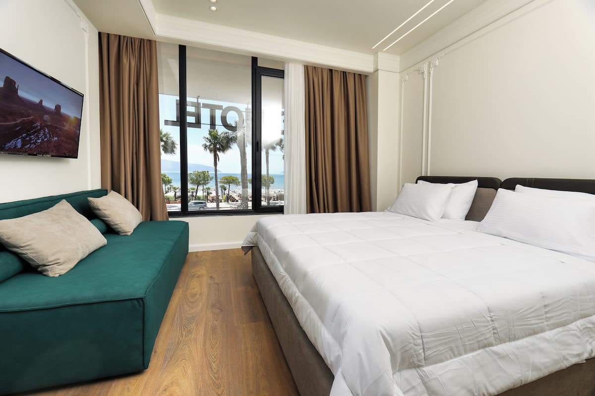 A hotel room with a bed, a green sofa, and a large window with curtains.