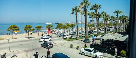 Une rue côtière bordée de voitures garées, de palmiers et offrant une vue sur la mer.