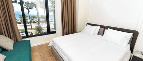 A hotel room with a large bed, a green sofa, and a view of the beach and palm trees.