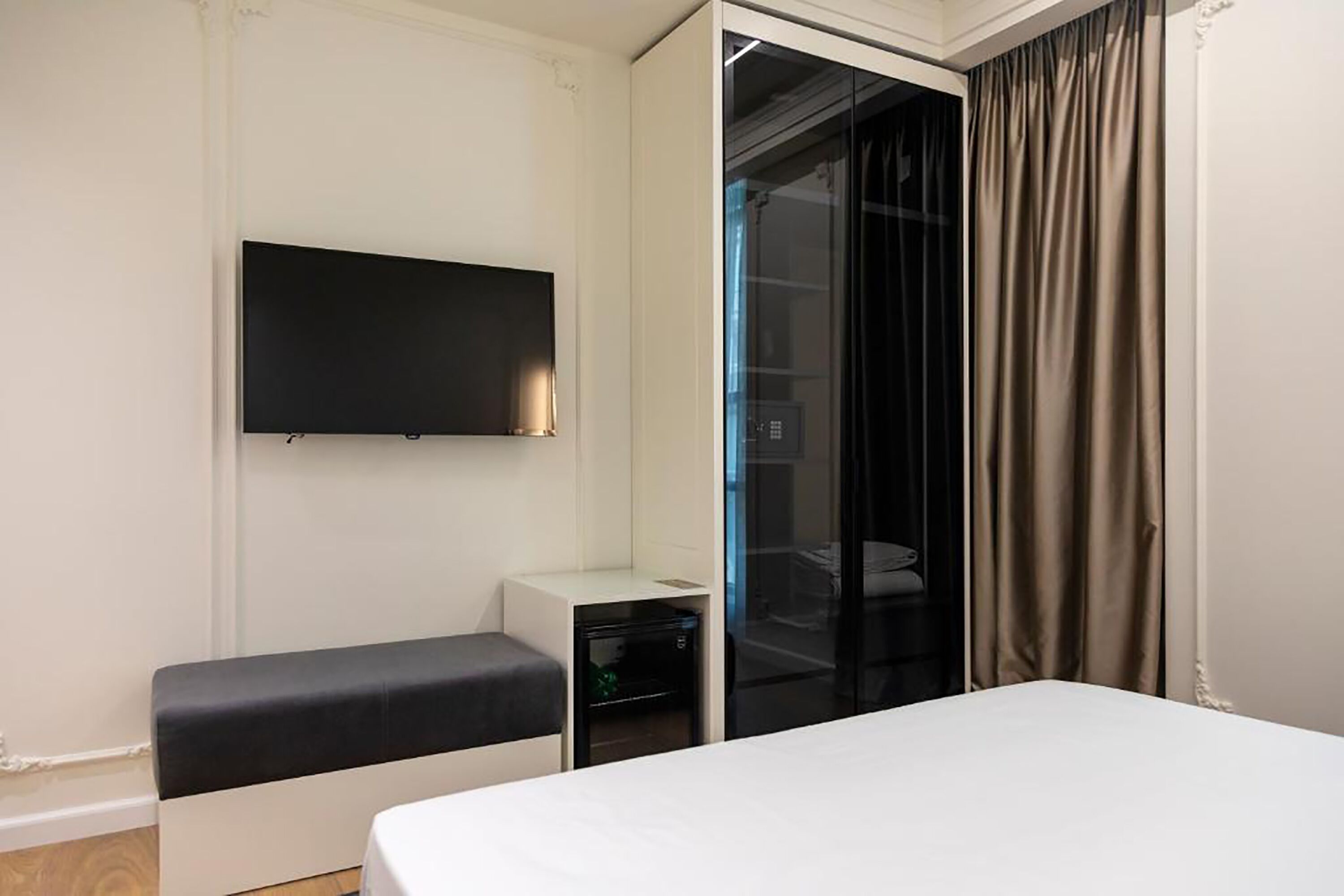 Une chambre d’hôtel moderne équipée d’un lit, d’un téléviseur à écran plat fixé au mur, d’une petite table de chevet et d’une porte-fenêtre coulissante donnant sur un placard.