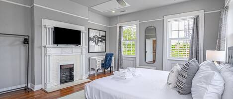 A bedroom with a fireplace, a bed with pillows, a desk, and a ceiling fan.
